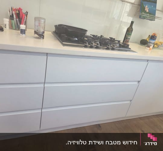 מטבח עם ארונות לבנים וכיריים על השיש